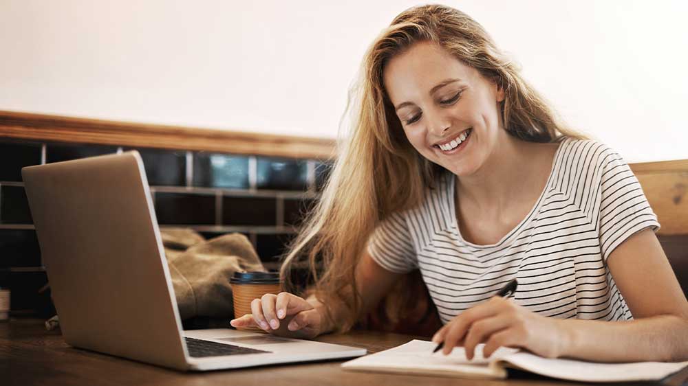 Mladá žena se věnuje studiu na notebooku a zapisuje si poznámky do sešitu_03