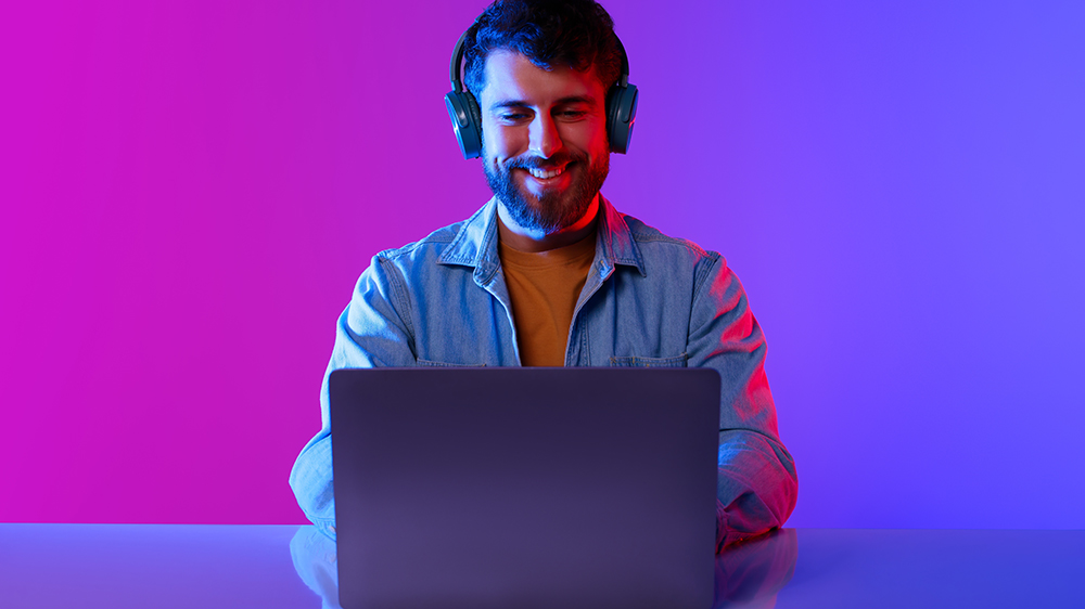 Mladý muž se sluchátky na uších hraje hry na notebooku Acer Nitro V 16 NH.QP1EC.003_06