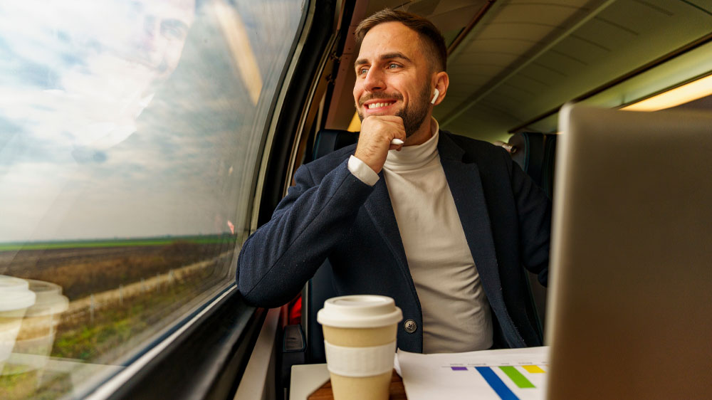 Muž jede ve vlaku, kouká z okna a před sebou kávu a notebook_03