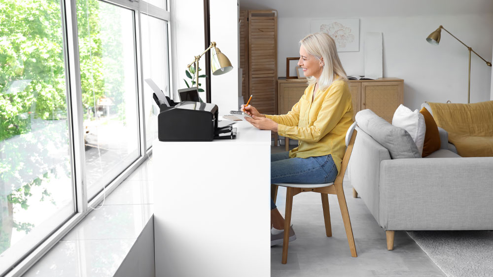 Žena u psacího stolu v ložnici před velkým oknem pracuje na notebooku_05