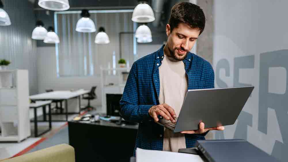 Muž stoj&iacute;c&iacute; u tisk&aacute;rny pracuje na notebooku_02