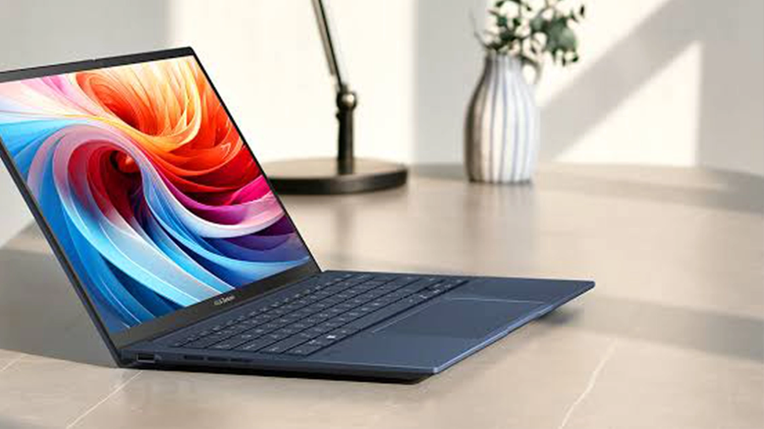 Stůl s lampičkou a květinou za notebookem ASUS