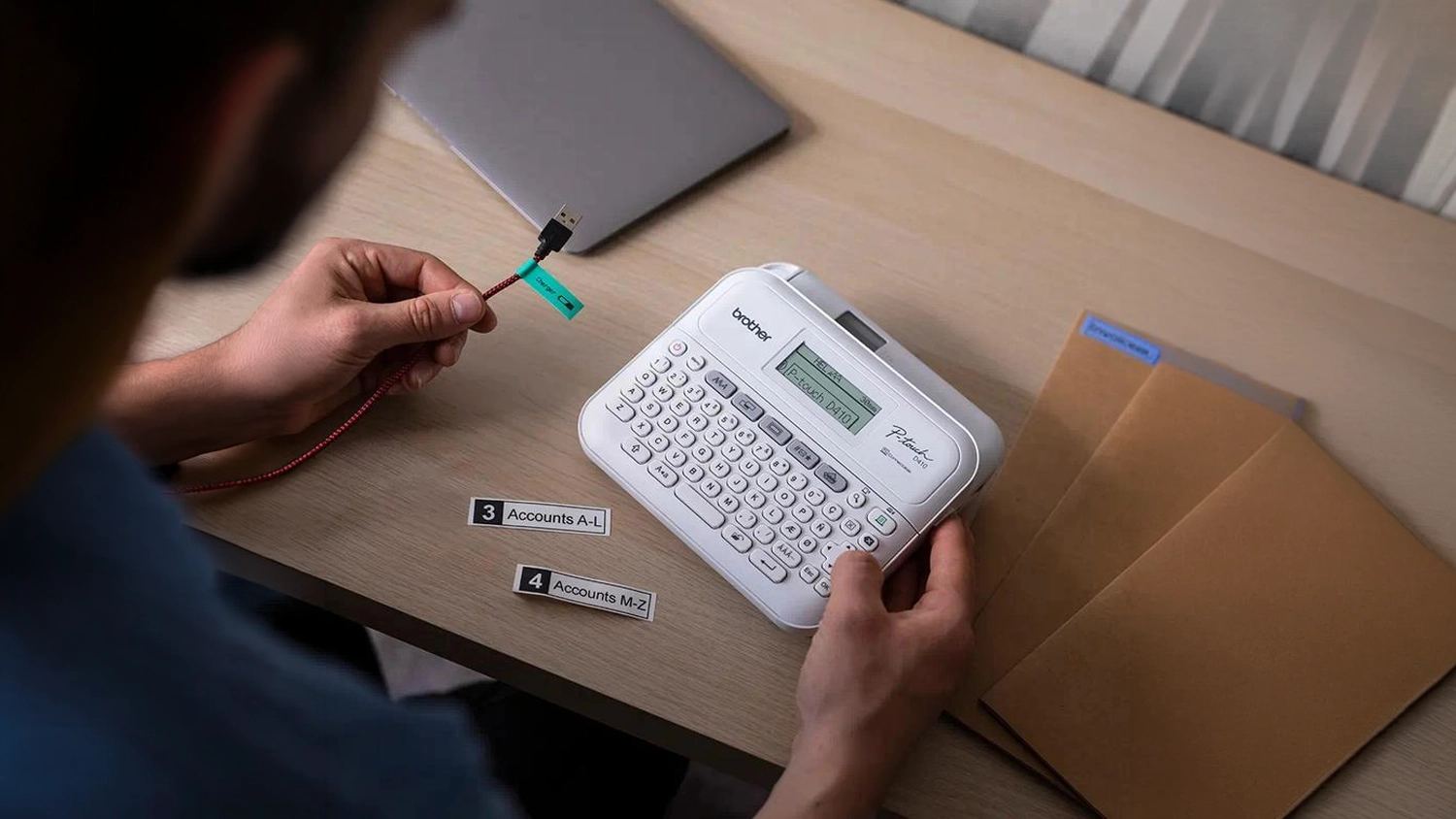Muž tiskne &scaron;t&iacute;tky u stolu s tisk&aacute;rnou &scaron;t&iacute;tků Brother PT-D410