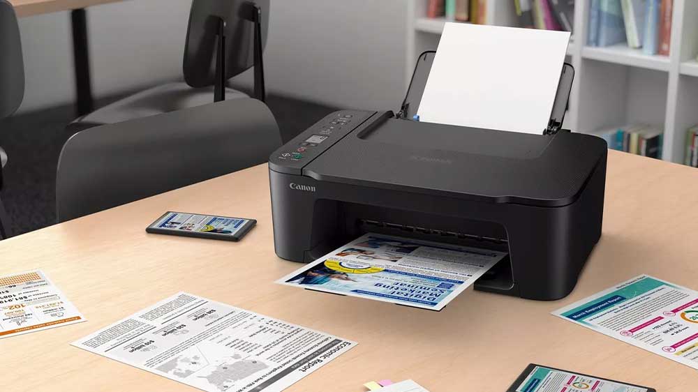 Tiskárna Canon Pixma TS9750I na stole mezi vytisknutými papíry_02