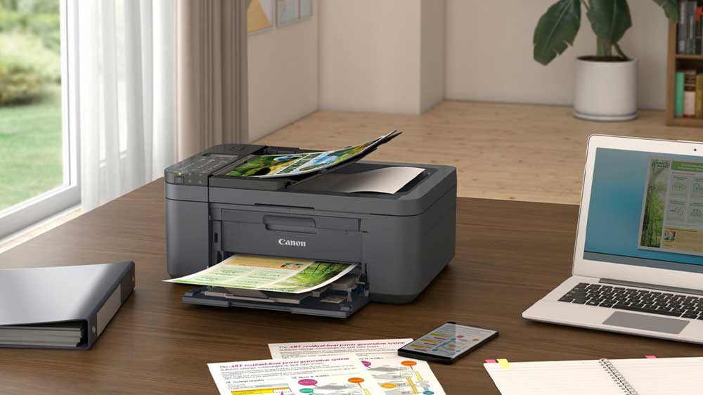 Tiskárna Canon PIXMA TR4755i na kancelářském stole vedle notebooku a telefonu_02