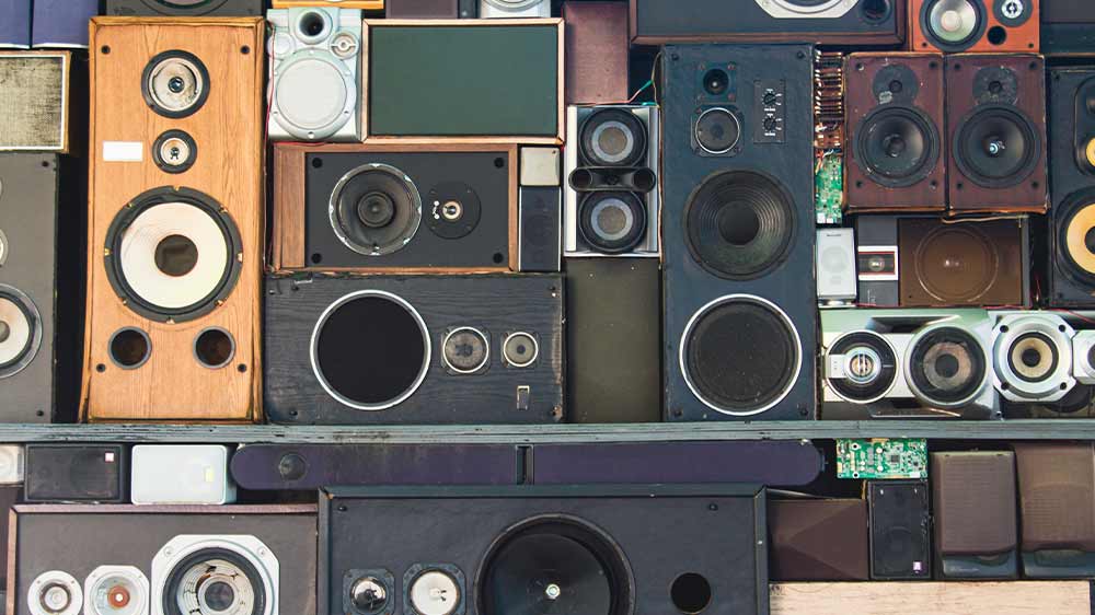 Ruka ukazující palec nahoru nad mixážním pultem ve studiu a v pozadí reproduktory_03