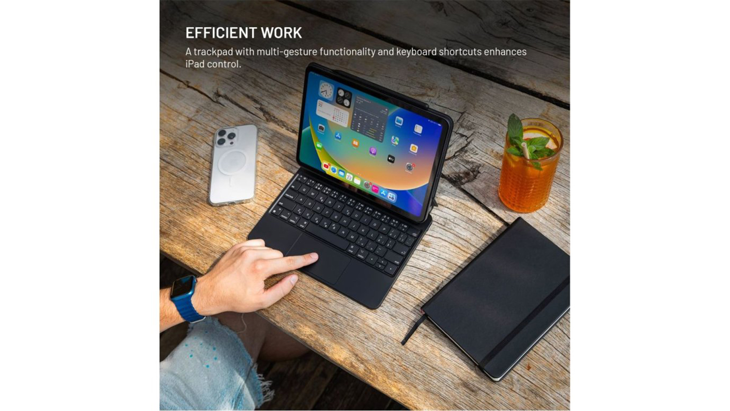 Ruka ovládající tablet uložený v pouzdru s klávesnicí FIXED Typee, na stole vedle mobilu, diáře a skleničky