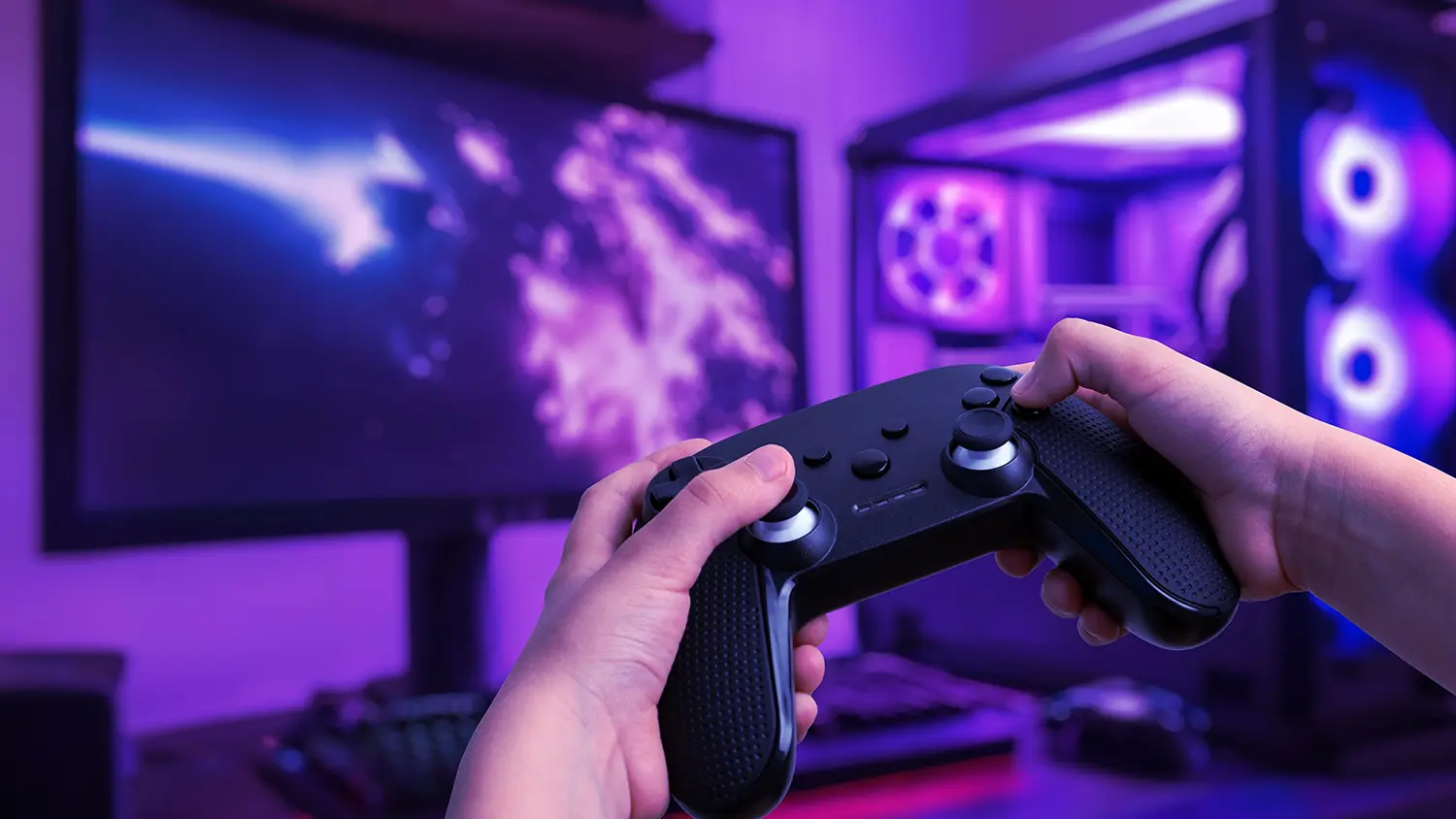 Muž drž&iacute;c&iacute; gamepad před poč&iacute;tačem