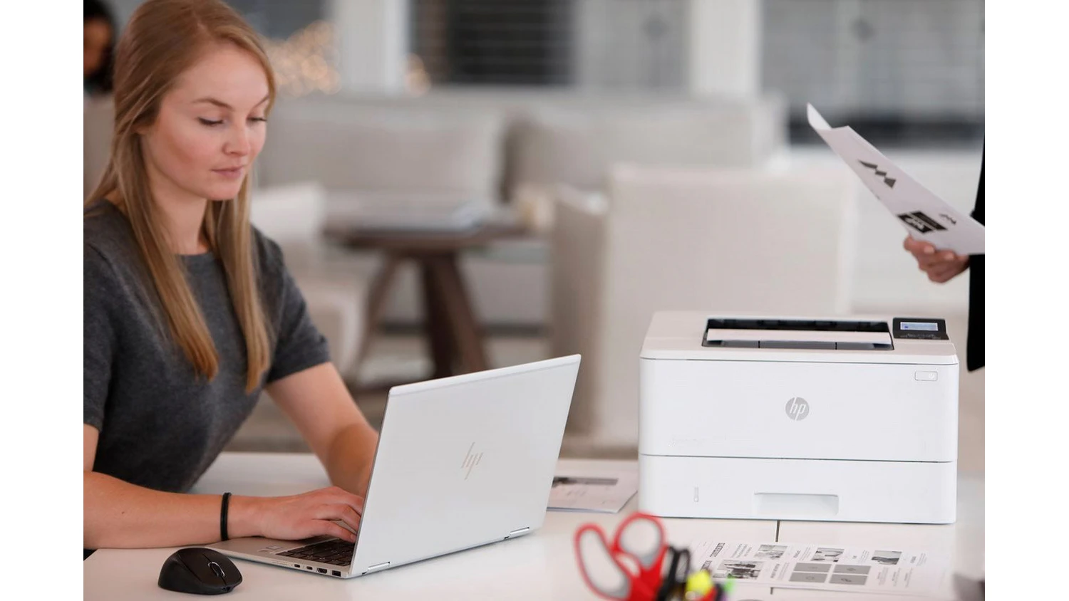Žena píše do notebooku vedle tiskárny HP LaserJet