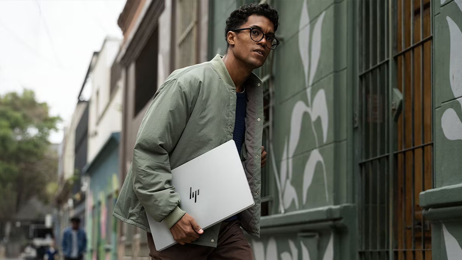 Muž ide po ulici s notebookom HP OmniBook 7