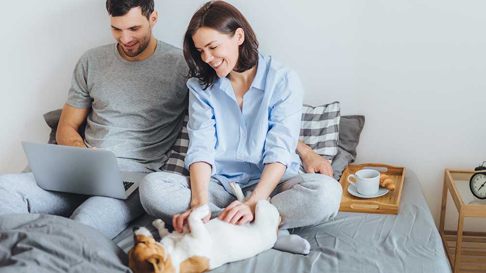 Mladý pár sedí na posteli a sleduje videa na notebooku Lenovo ThinkBook 16 G7 ARP. Žena přitom hladí pejska typu Jack Russell_03