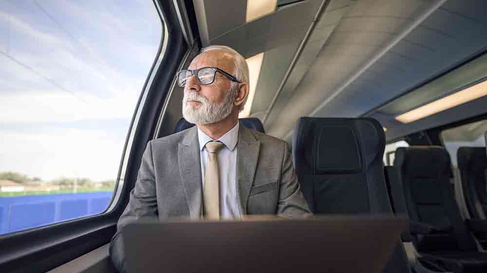 Starší muž pracuje na notebooku během cestování vlakem_04