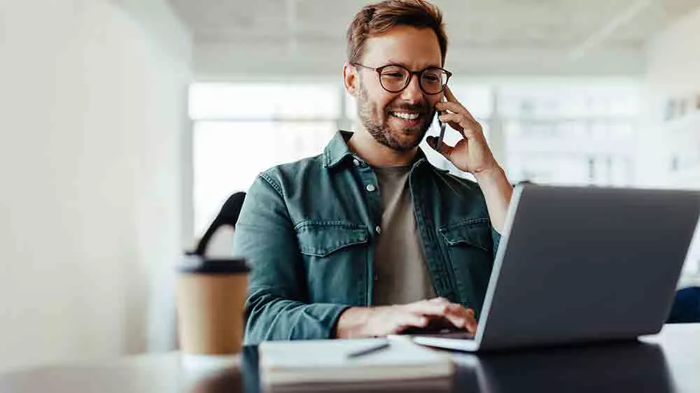 Muž pracuje na notebooku a telefonuje