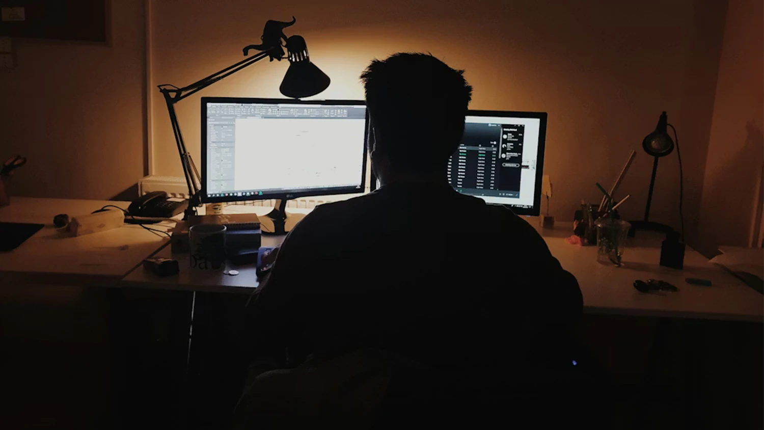 Osoba u pracovn&iacute;ho stolu s monitory a lampičkou