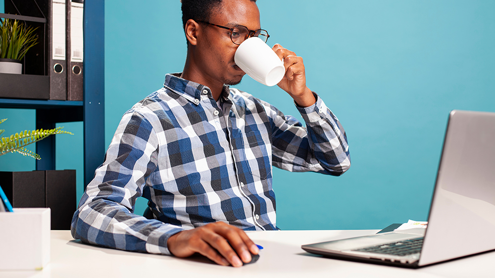 muž na modrém pozadí pije kávu a pracuje na laptopu