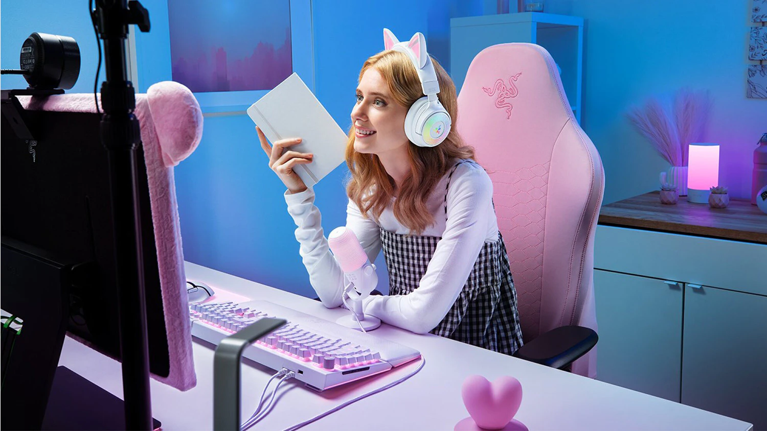 Mladá žena sleduje obrazovku počítače s nasazenými sluchátky Razer Kraken Kitty V3 Pro v bílé barvě.