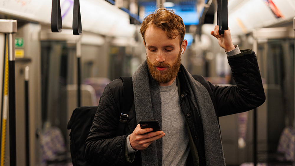 Muž cestující metrem s batohem na zádech s mobilním telefonem v ruce a sluchátky v uších_03