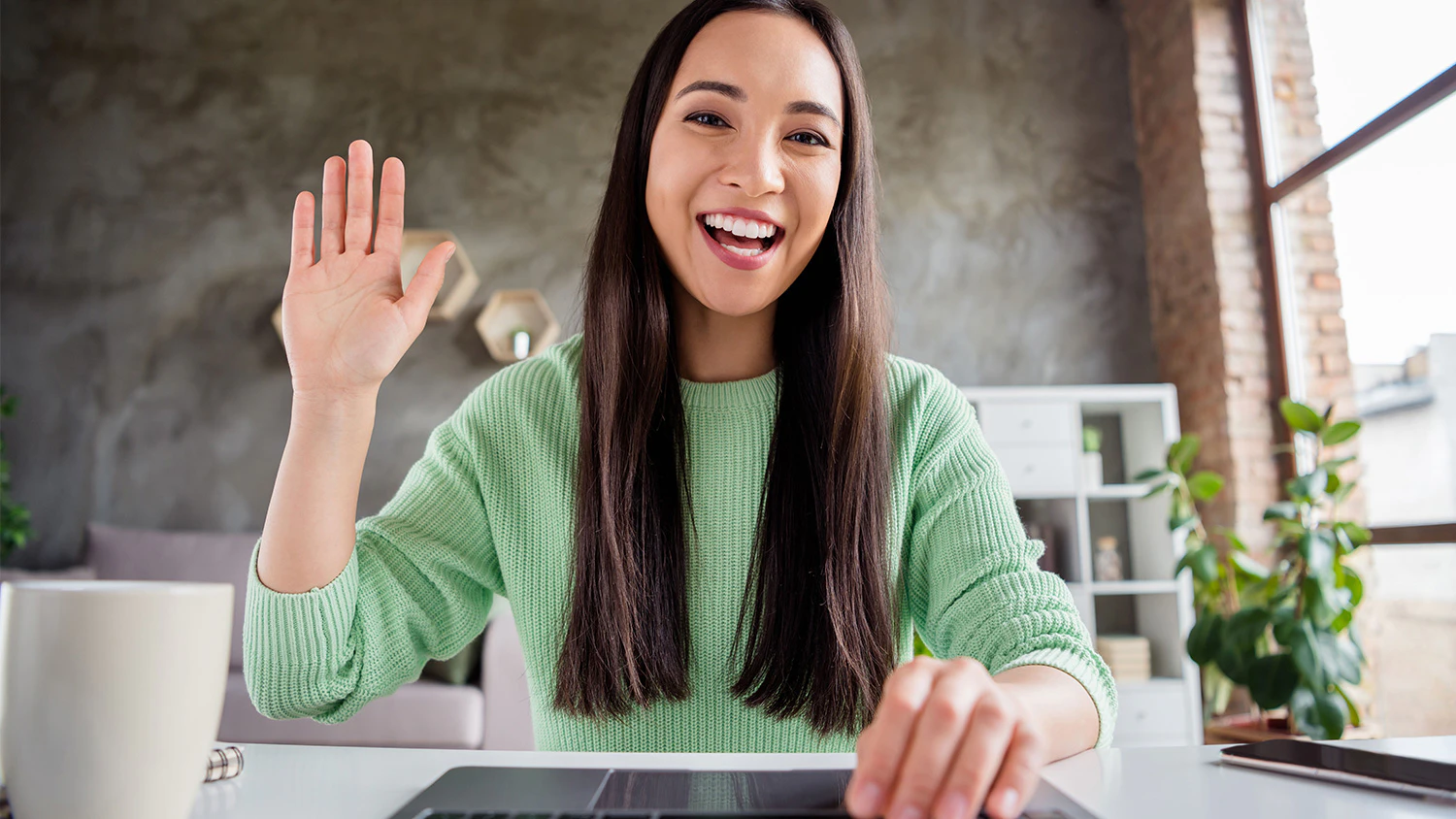 Usm&iacute;vaj&iacute;c&iacute; se a m&aacute;vaj&iacute;c&iacute; žena za stolem u kl&aacute;vesnice pohledem z obrazovky či monitoru