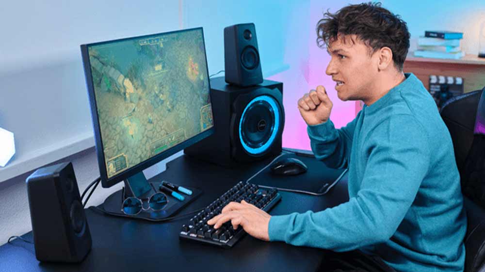 Muž hraje akční počítačovou hru a na stole má reproduktory Trust GXT 629 Tytan RGB 2.1_02