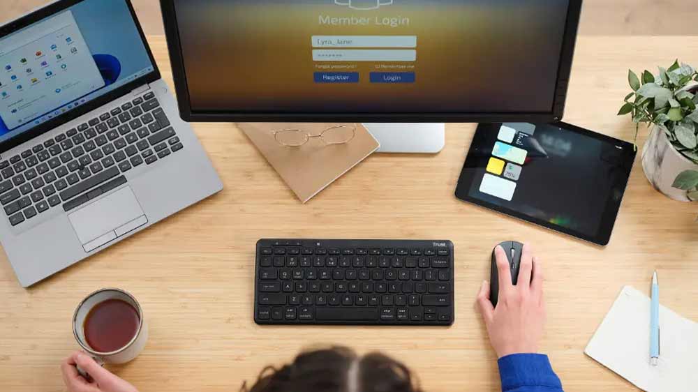 Žena má na pracovním stole počítač, notebook a tablet a bezdrátově připojenou klávesnici Trust LYRA Wireless US_02