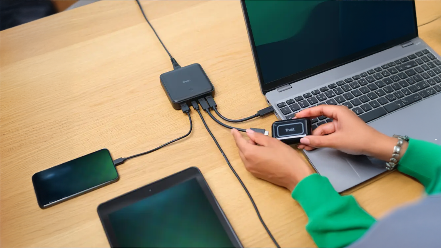 Nap&aacute;jec&iacute; adapt&eacute;r Trust Maxo USB-C/USB-A 100W se zapojen&yacute;mi 4 zař&iacute;zen&iacute;mi na stole
