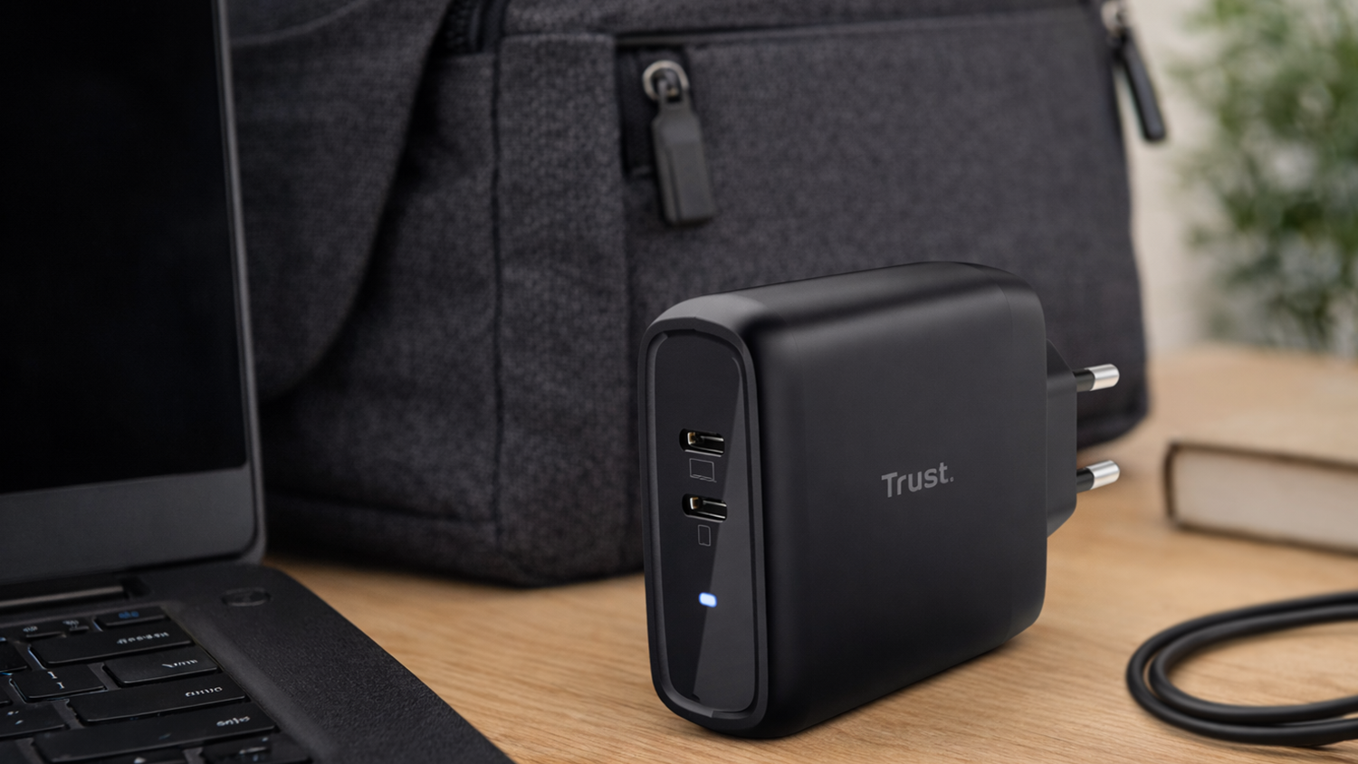 Napájací adaptér Trust Maxo Dual 65W ležiaci na pracovnom stole vedľa notebooku