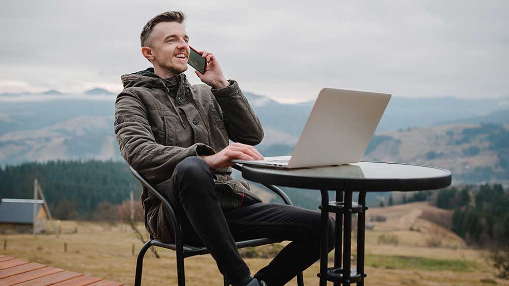 Usmívající se žena, která venku kouká na mobil a má připravený notebook na práci_02