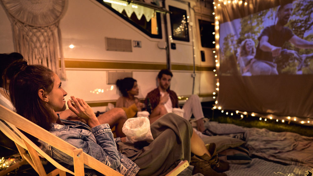 Skupina mladých lidí sledujících film na plátně venku v přírodě_02