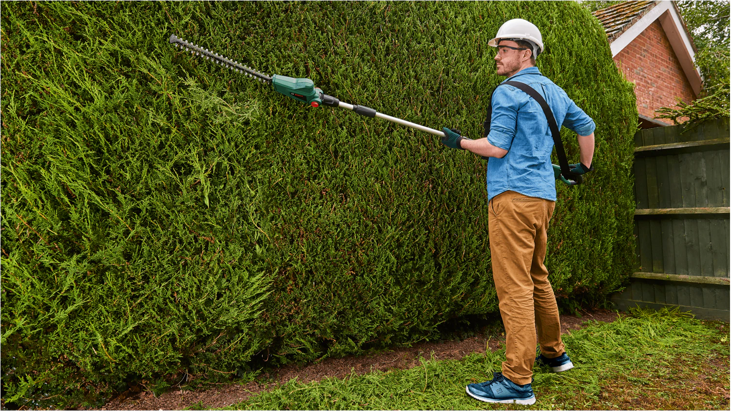 Muž používající akumulátorové nůžky na živý plot Bosch UniversalHedgePole 18