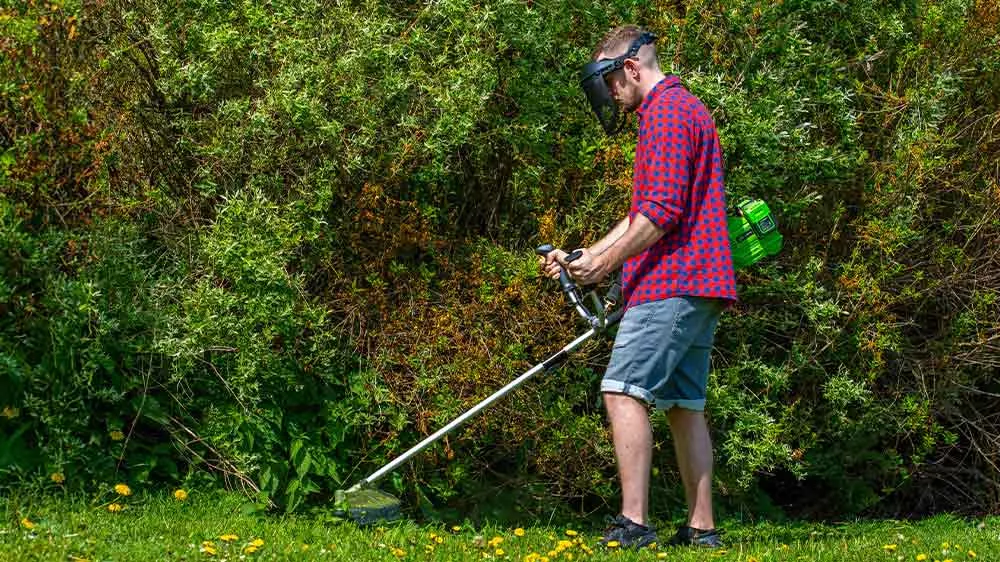 Muž s krovinorezom Fieldmann upravuje z&aacute;hradu