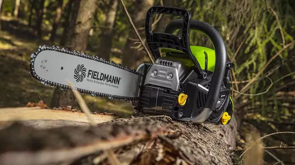 Benzínová píla Fieldmann položená na kmeni stromu