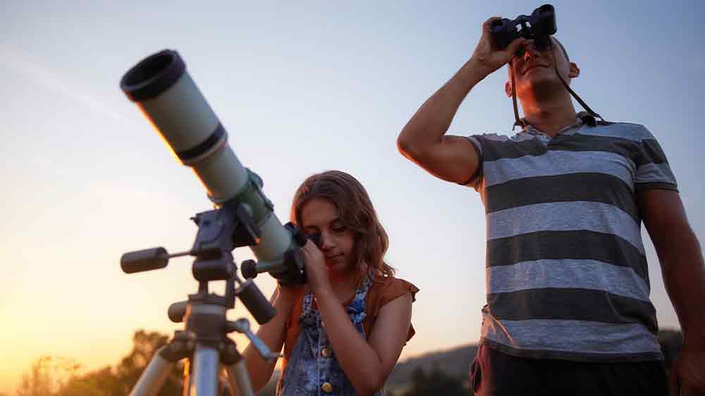 Malé dievčatko sa pozerá do ďalekohľadu umiestneného na statíve _02