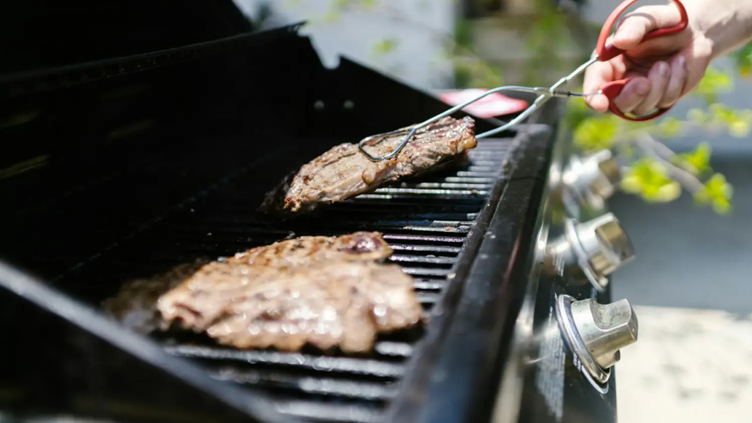 Detail na ruku s kleštěmi, která obrací maso na grilu