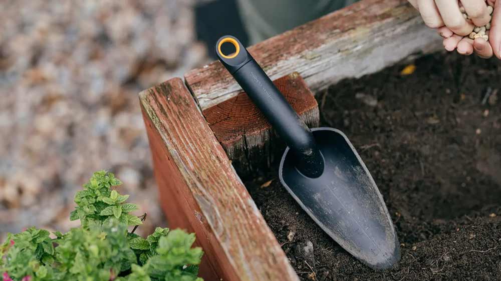 Člověk s&aacute;zej&iacute;c&iacute; sem&iacute;nka do květin&aacute;če, na kter&eacute;m lež&iacute; lopatka Fiskars Solid_02