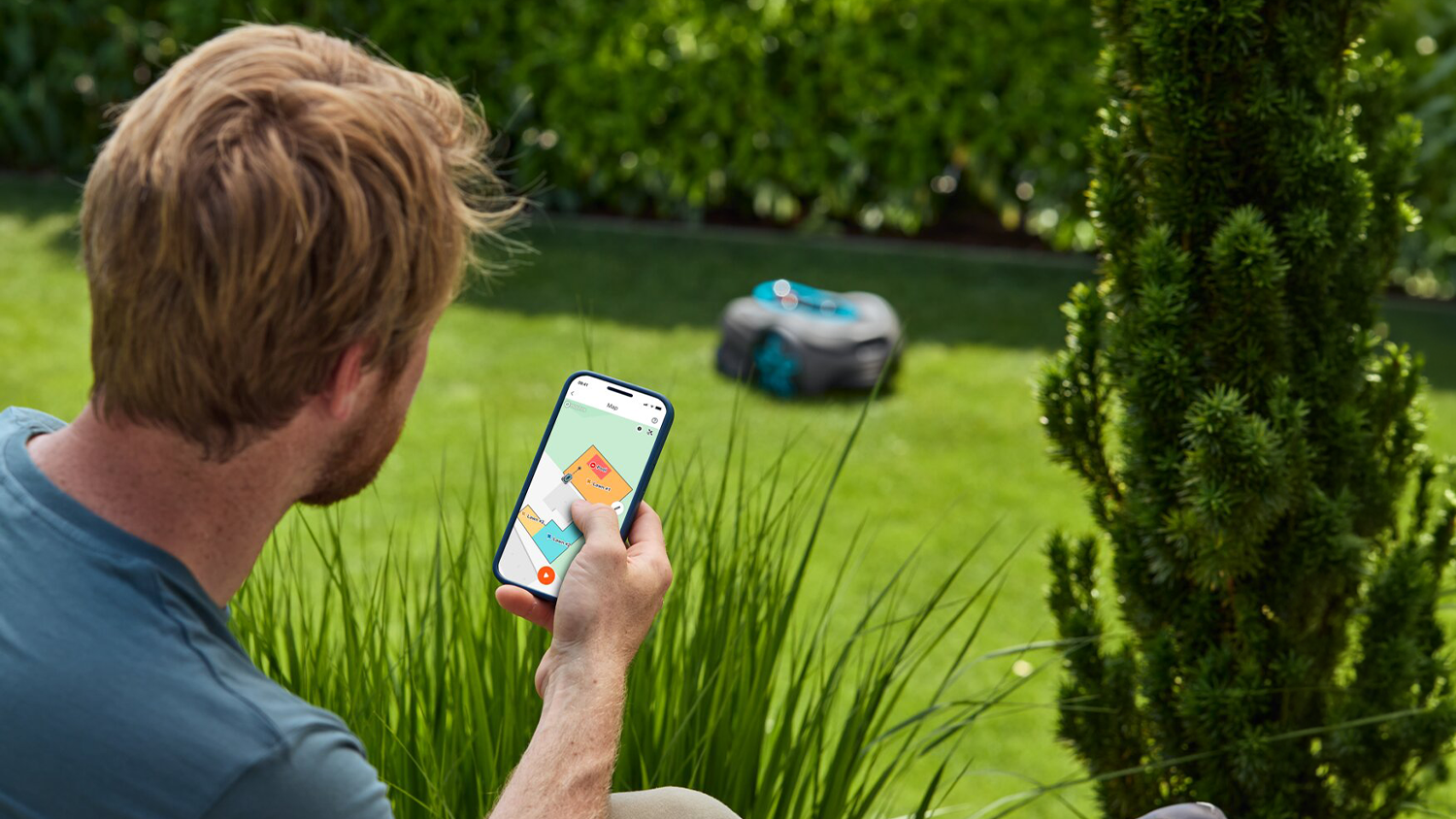 Muž ovládá sekačku přes aplikaci v mobilu