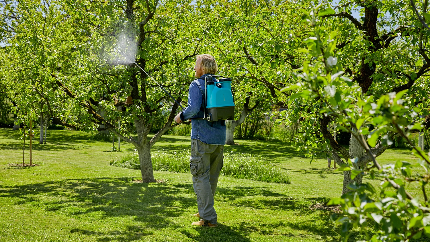 Muž stříká stromy v zahradě s postřikovačem GARDENA