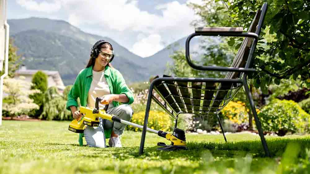 Žena upravuje trávník pod lavičkou na zahradě se strunovou zahradní sekačkou Kärcher LTR 3-18 Dual Battery Set_03