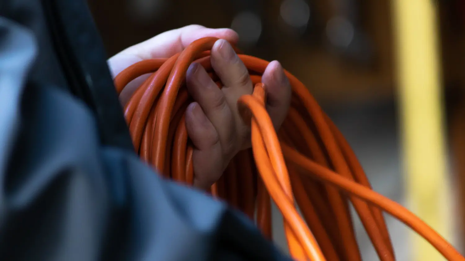 Muž drží v ruke oranžový predlžovací kábel.