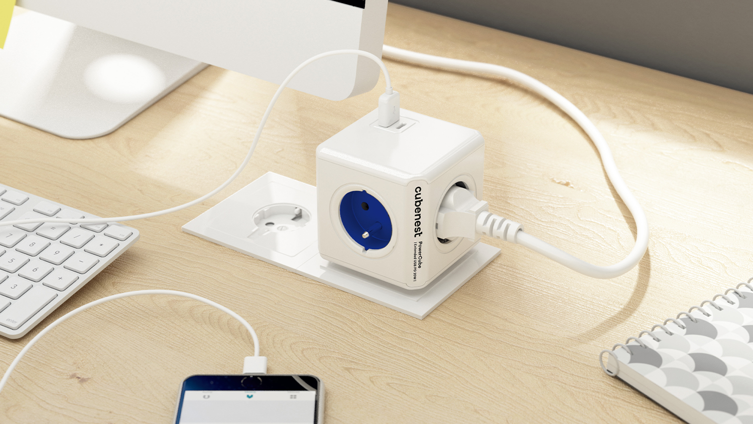 Rozbočovač do zásuvky s USB porty CUBENEST PowerCube Original modrá na stole s připojeným mobilem