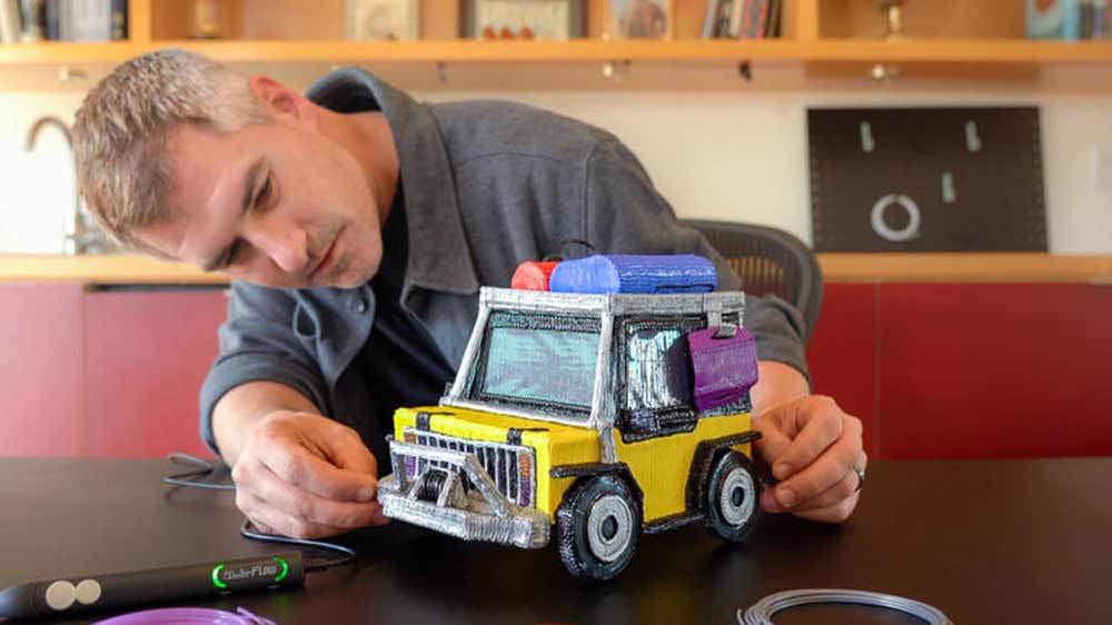 Muž prohlížející si postavený model automobilu pomocí 3D pera 3Doodler FLOW+, které leží na stole_04