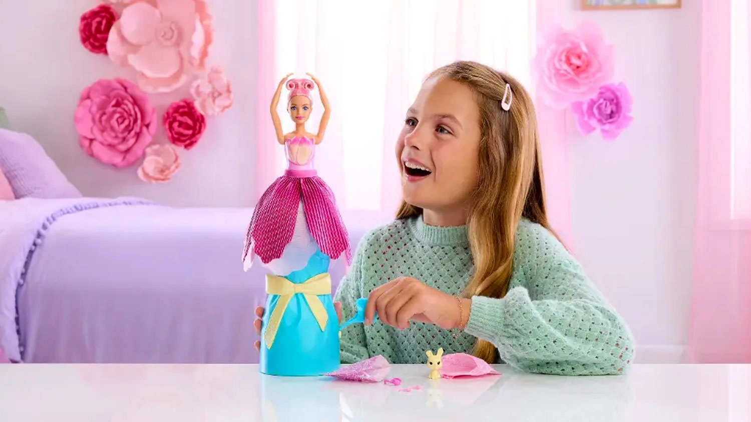 Nadšená dívka si hraje s panenkou Barbie Petal Pop růžový tulipán, která se vysouvá z modrého podstavce s mašlí.