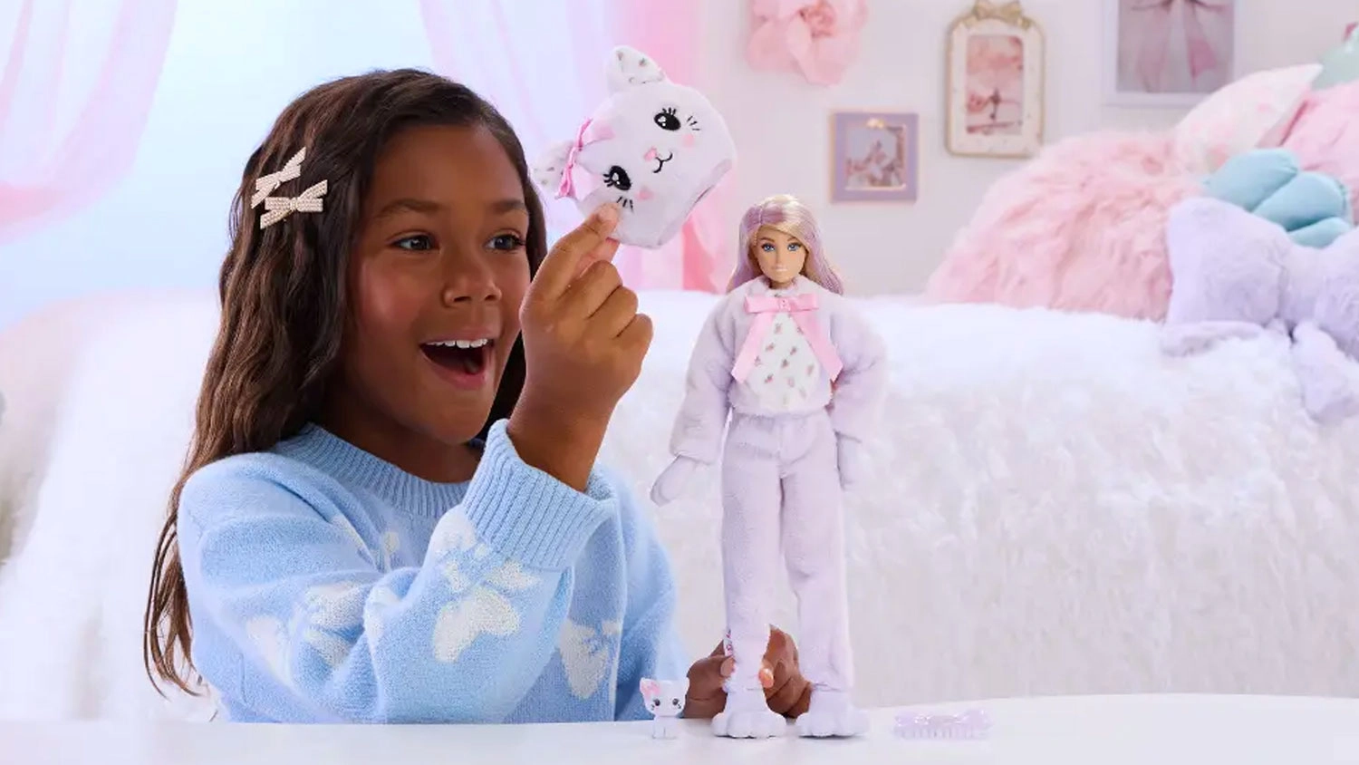 Dívka drží plyšovou hlavu koťátka vedle panenky Barbie Cutie Reveal ve fialovém plyšovém kostýmu a malého bílého mazlíčka.