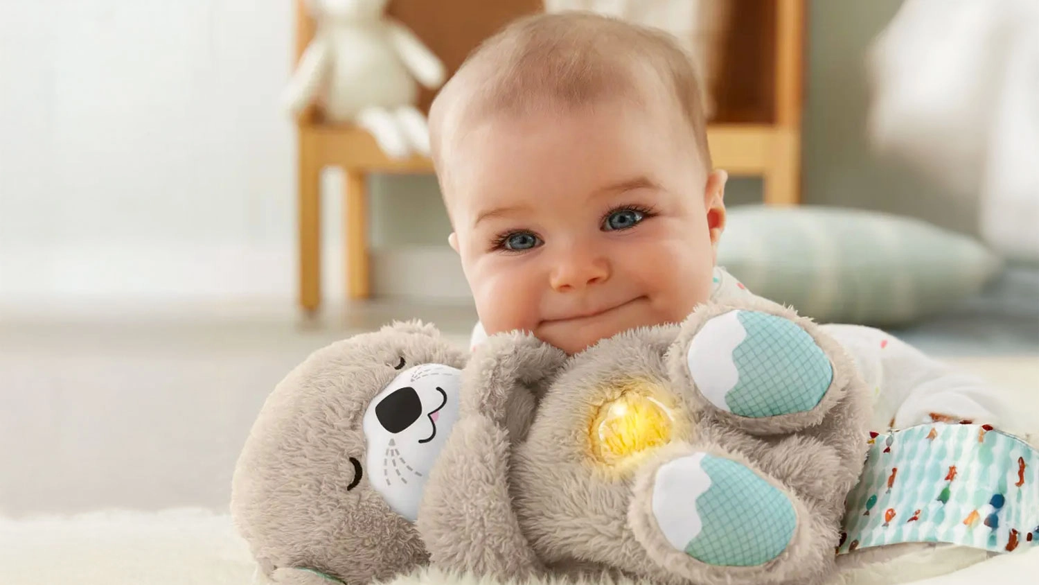 Usm&iacute;vaj&iacute;c&iacute; se miminko lež&iacute; s ply&scaron;ovou zklidňuj&iacute;c&iacute; vydrou Fisher-Price, kter&aacute; m&aacute; jemně rozsv&iacute;cen&eacute; bř&iacute;&scaron;ko.