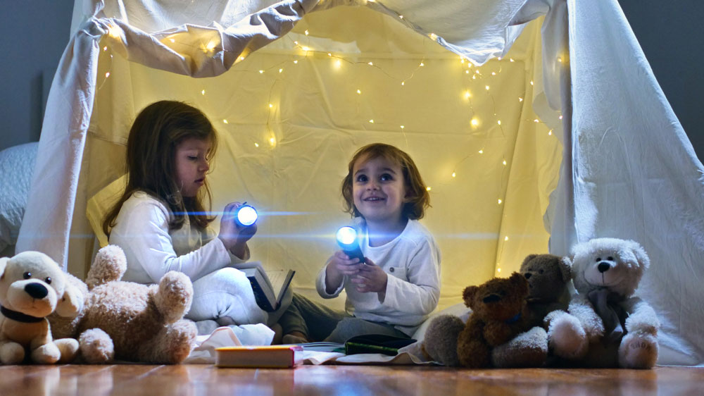 Dvě mal&eacute; holčičky v improvizovan&eacute;m stanu doma s rozsv&iacute;cen&yacute;mi baterkami v ruce_02