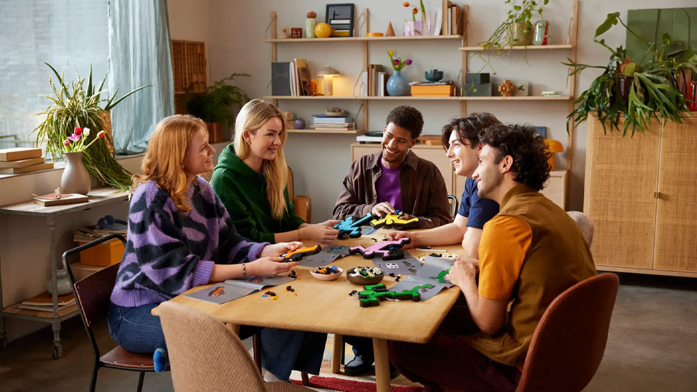 Přátelé sedící u stolu sestavují s radostí jednotlivé figurky ze stavebnice LEGO® Art 31216 Keith Haring – Tančící postavy_02