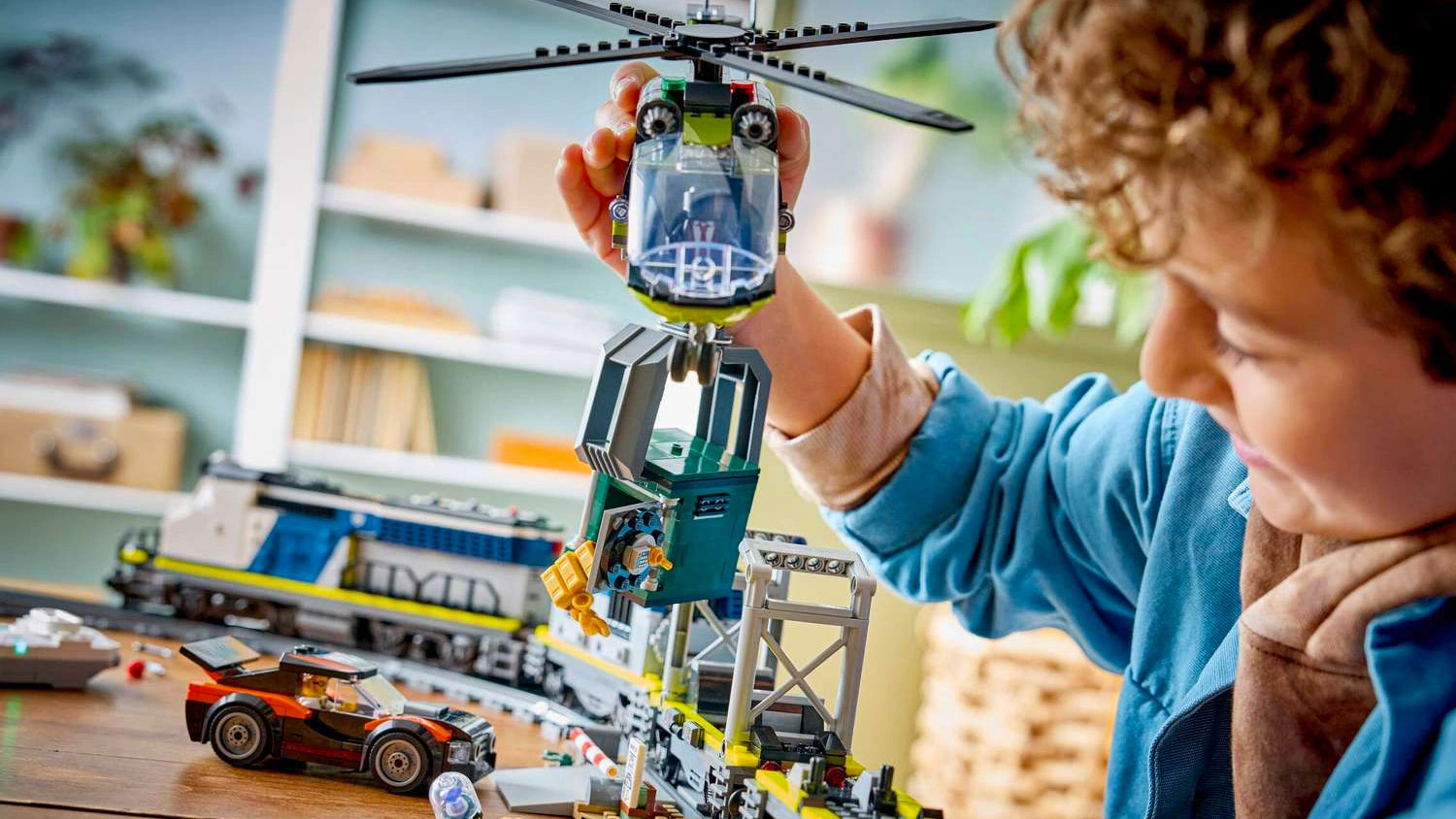 Usmívající se chlapec drží v ruce helikoptéru ze stavebnice LEGO® City 60508 Loupež v policejním vlaku a s pomocí drapáku zvedá trezor