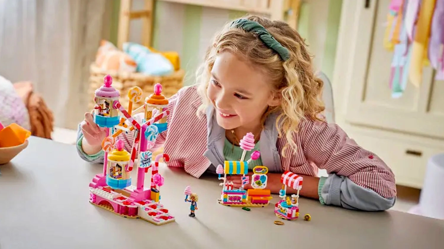 Dievčatko stavia kocky LEGO® Friends 42700 Kolotoč so sladkosťami a cupcakmi