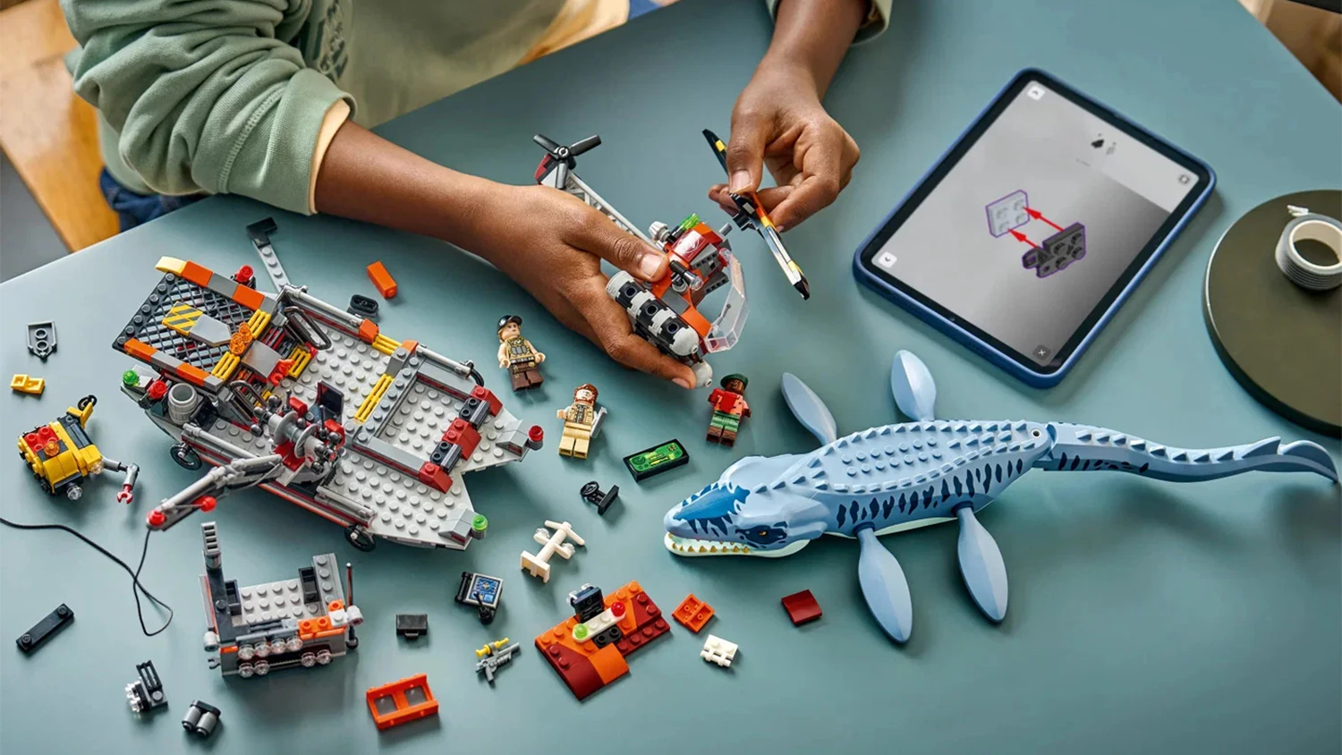 Chlapec skl&aacute;daj&iacute;c&iacute; stavebnici LEGO&reg; Jurassic World 77983 &Uacute;tok dinosaura mosasaura na loď