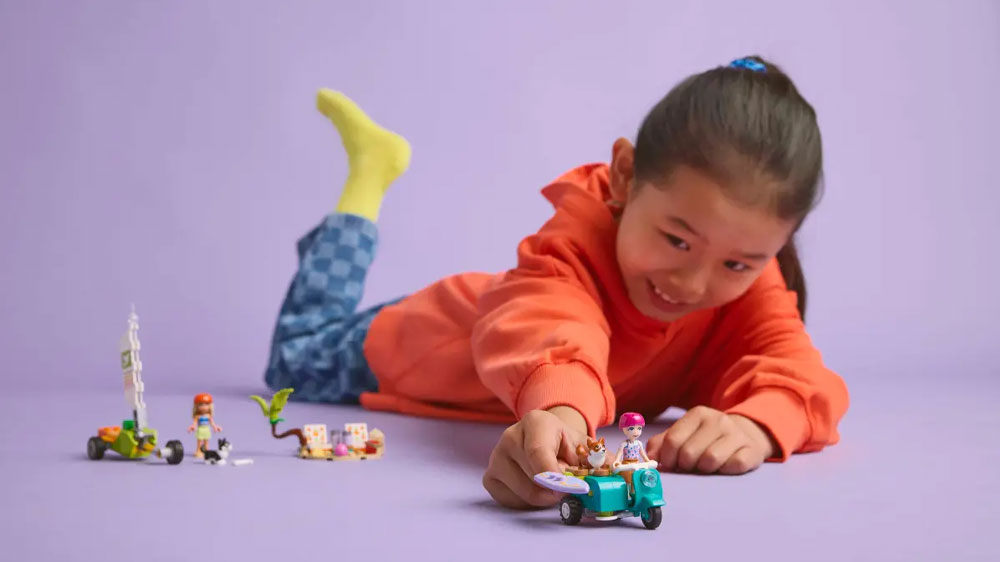 Veselá dívka si hraje s LEGO® Friends 42641 Dobrodružství se surfujícími psy a skútrem a vozí pejska a minipanenku na skútru_02