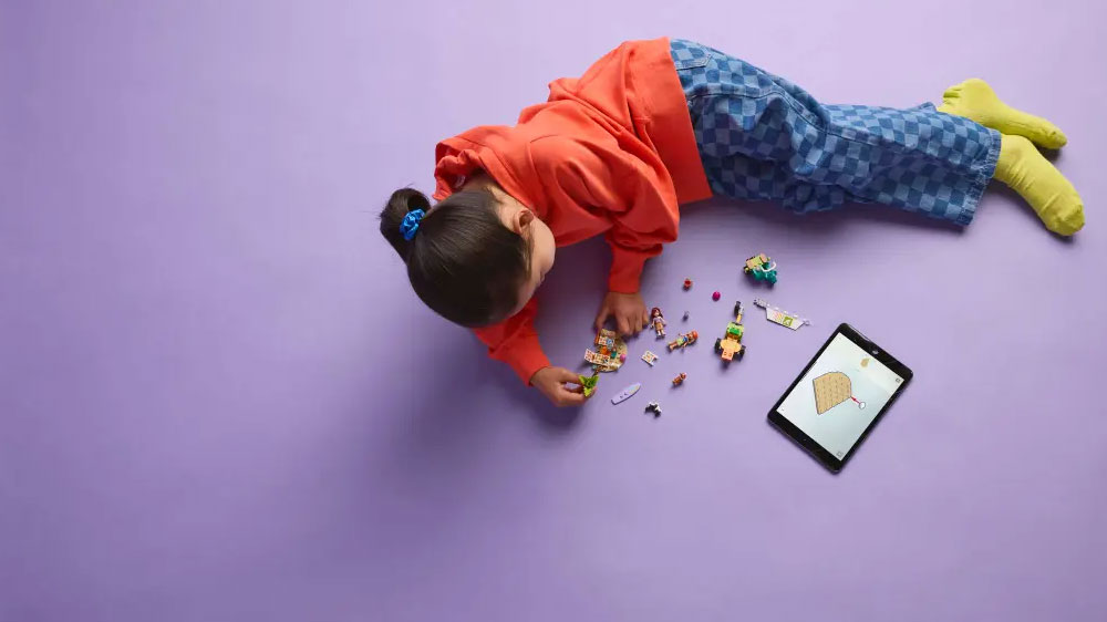 Dívka sestavuje LEGO® Friends 42641 Dobrodružství se surfujícími psy a skútrem a na tabletu má otevřenou aplikaci LEGO® Builder_04